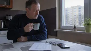 Mężczyzna z kubkiem kawy wpatruje się w dokumenty. Zastanawia się: co jeśli ktoś zna mój PESEL? Obok leżą okulary i telefon.