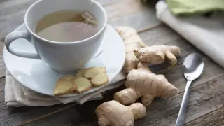 Kubek z herbatą imbirową, plasterki imbiru i korzenie na drewnianym stole. Czy imbir można pić codziennie?