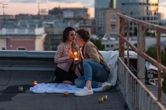 Romantyczny wieczór na dachu. Para trzyma świece, a w tle widać miasto. Zastanawiasz się, co napisać chłopakowi, jeśli nie odpisuje? Może taka chwila rozmowy jest lepsza?